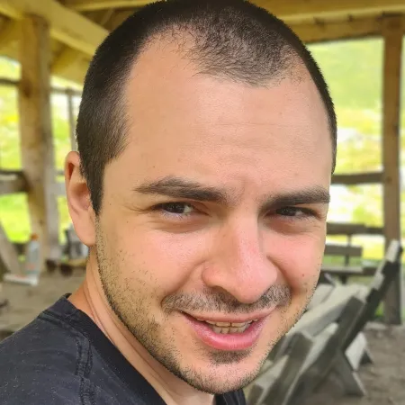 Hombre joven con sonrisa ligera bajo un refugio de madera al aire libre