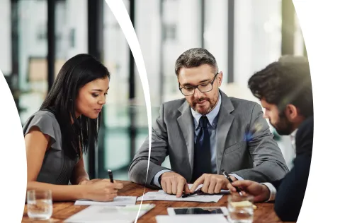 Three business professionals collaborating at a table, reviewing documents and discussing strategy.