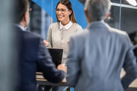 Three professionals working together at a computer, smiling and reviewing lines of code displayed on a large screen.