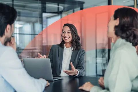 Smiling businesswoman leading a discussion with colleagues around a laptop during a meeting.