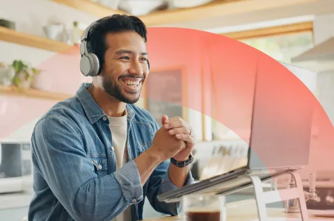 Smiling professional participating in a video meeting on a laptop from home, and wearing headphones