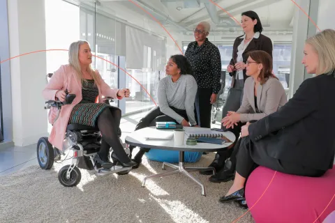 Diverse group of professionals having a meeting, with one person in a wheelchair leading the discussion.