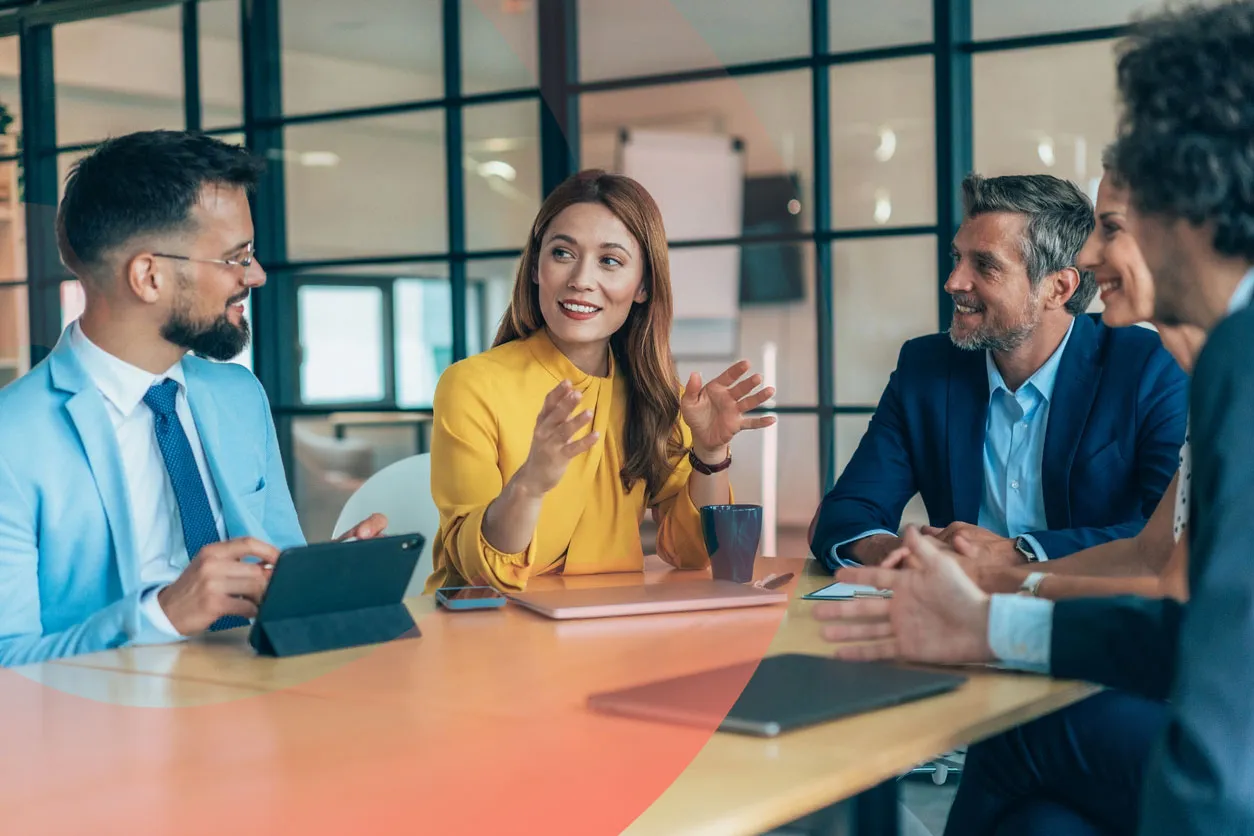 Four professionals sitting around a table, with one woman leading the discussion while others listen and smile.