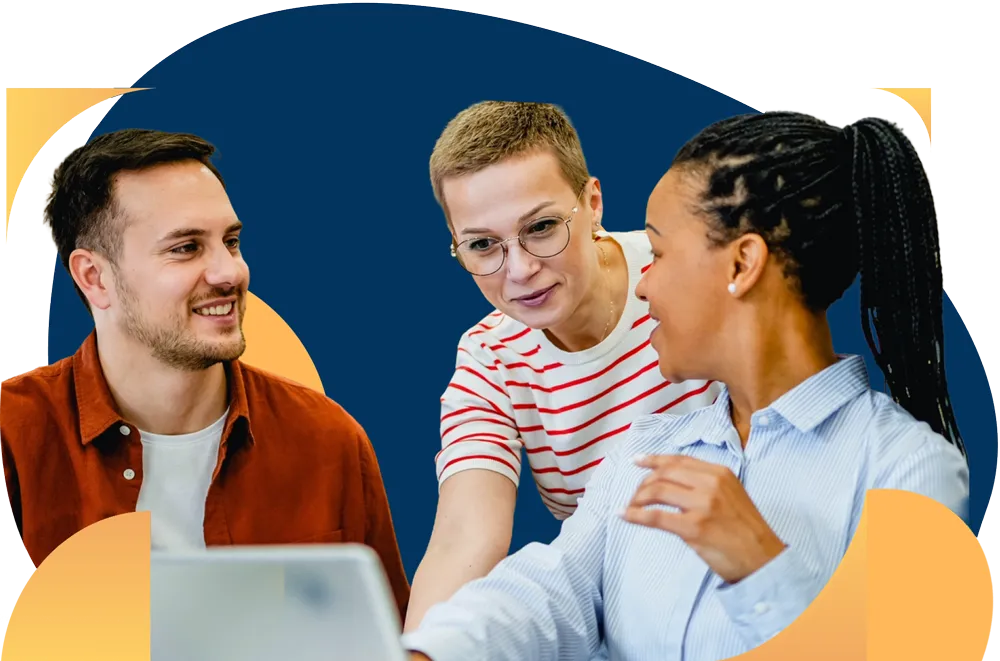 Three coworkers smile while collaborating around a laptop in an office setting