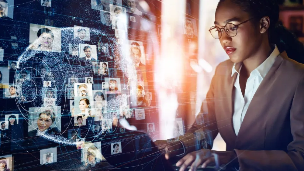 Professional at desk viewing digital interface with floating profile images and glowing light effect
