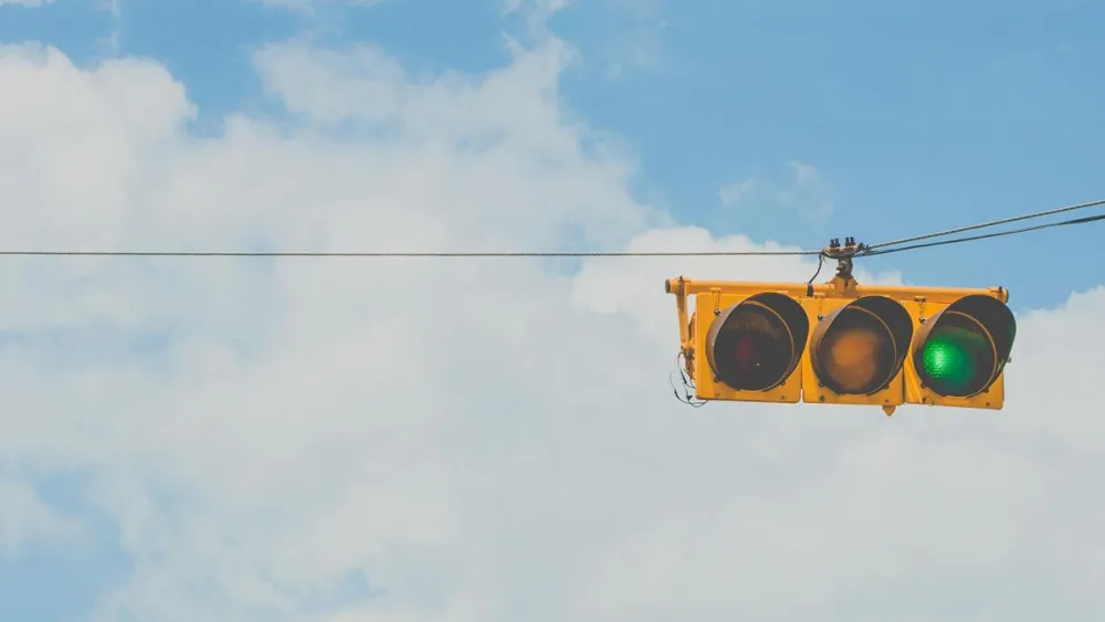 Yellow traffic light against blue cloudy sky. Green light is on signalling "Go"