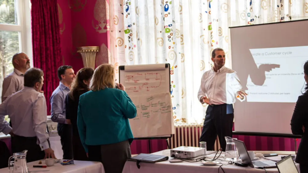 CUPE classroom - trainer stood infront of a projector with the audience stood beside him
