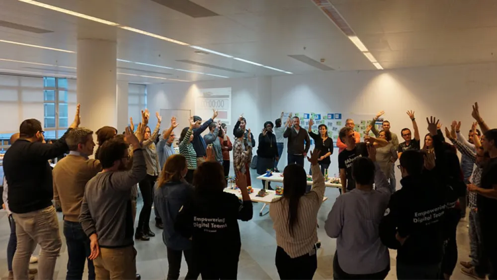 An AgilePM course in action - people stood in a circle with raised hands