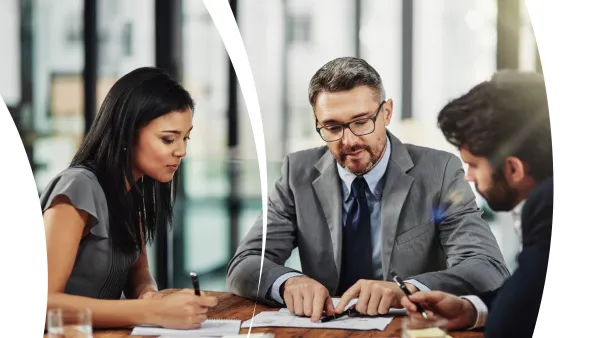 Three business professionals collaborating at a table, reviewing documents and discussing strategy.