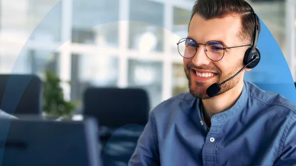 Smiling professional wearing a headset, looking at a computer monitor.