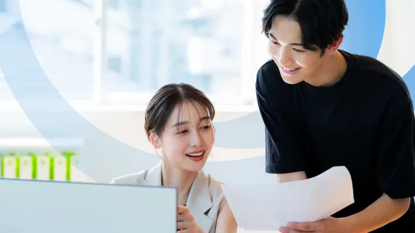 Two co-workers reviewing printed documents together at a computer